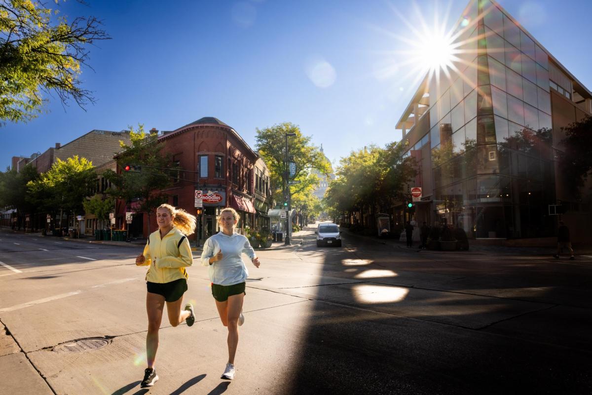 Two college aged women running in athletic wear on State Street on a sunny afternoon