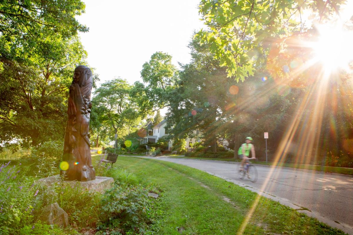 A bicyclist rides past the Native American memorial in Hudson Park. The memorial is a statue shaped as a totem featuring a wolf, bear, cub, lynx, thunderbird, eagle, and a Ho Chunk warrior