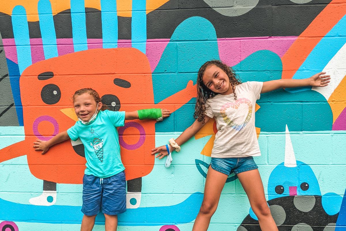 Two kids pose with a colorful mural