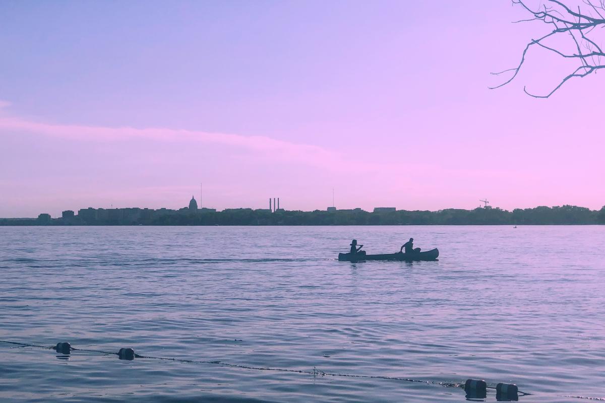 A canoe passes Olbrich Park with the Madison skyline in the background