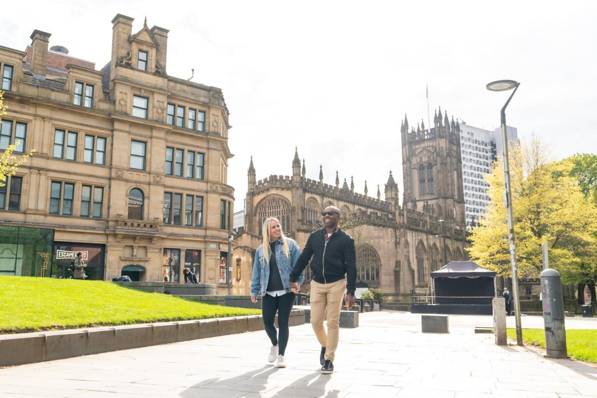 Couple walking outside Manchester Cathedral and Corn Exchange.