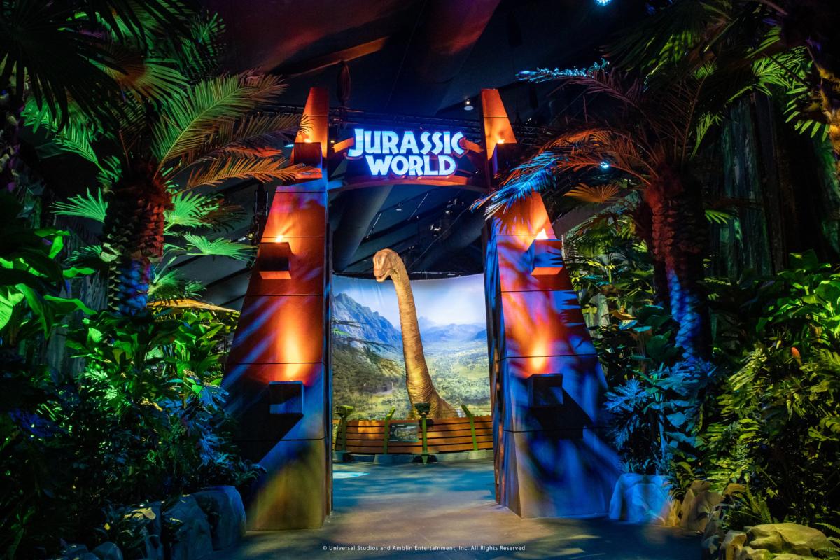 Gates at an attraction saying Jurassic World with a dinosaur in the background