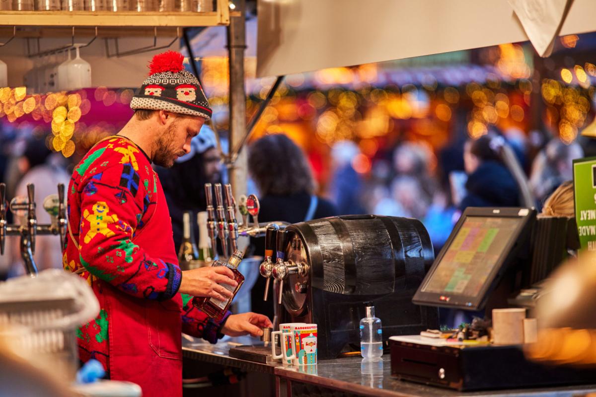 Man pouring drinnks at a christmas markets stall