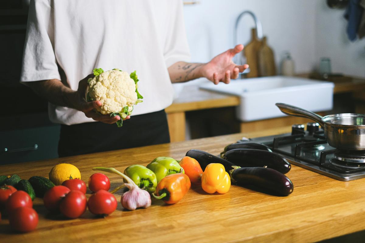 Person holding food with vegetables on chopping board and kitchen equipment