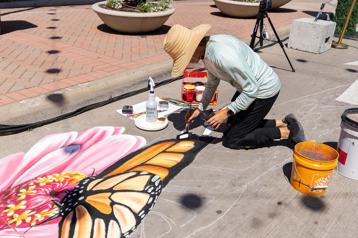 Artist creating 3D illusion of a butterfly on the road using chalk