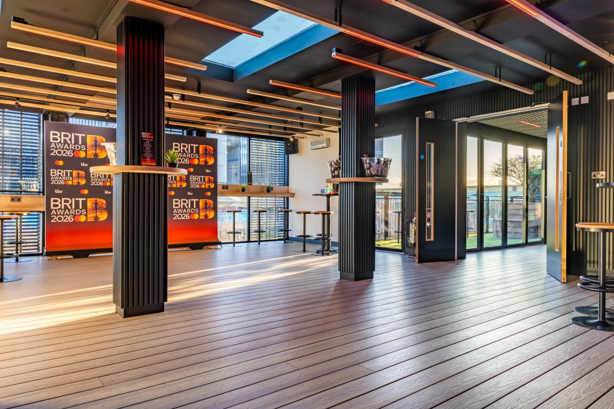 Wide interior view of Canalside at Co-op Live set up for the BRIT Awards 2026, showing a modern event space with wooden flooring, tall tables, feature lighting and branded BRIT Awards backdrops