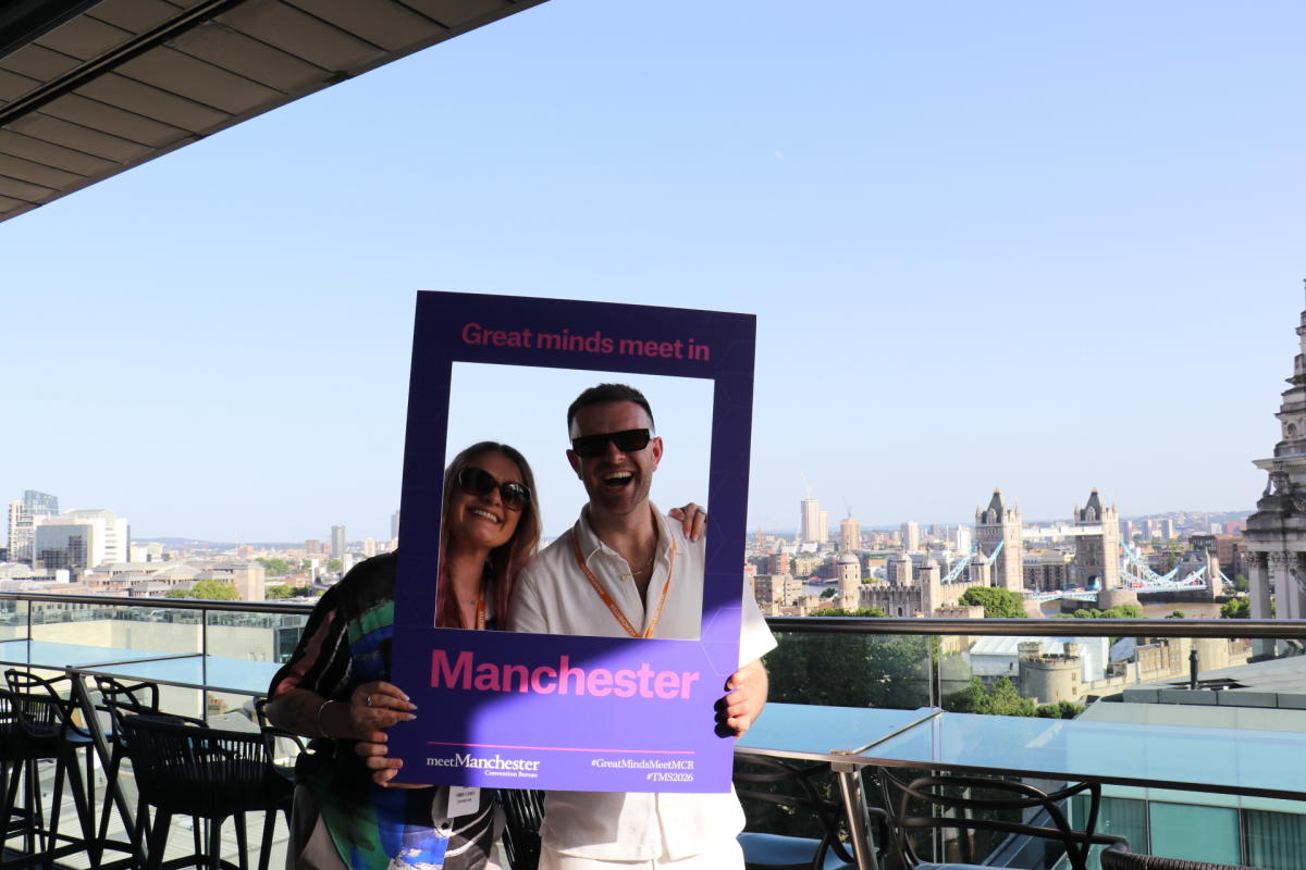 Two delegates pose with a branded Manchester photo frame on a rooftop terrace overlooking the London skyline during The Meetings Show 2026, with Tower Bridge visible in the background.