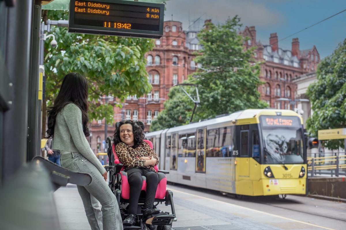 2 people waiting for a tram at St Peter's Square, with a yellow tram in the background.