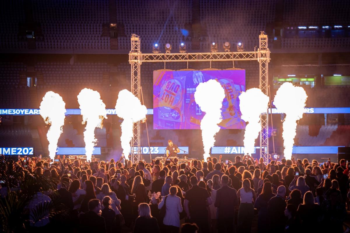 Crowd in front of stage with DJ and fireworks.