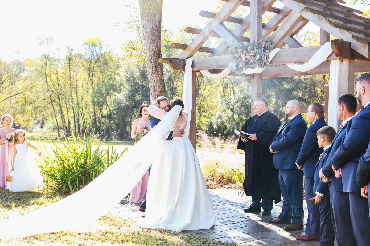 Bride And Groom Hugging In Front Of Family At Adam's Acres In Milledgeville, GA