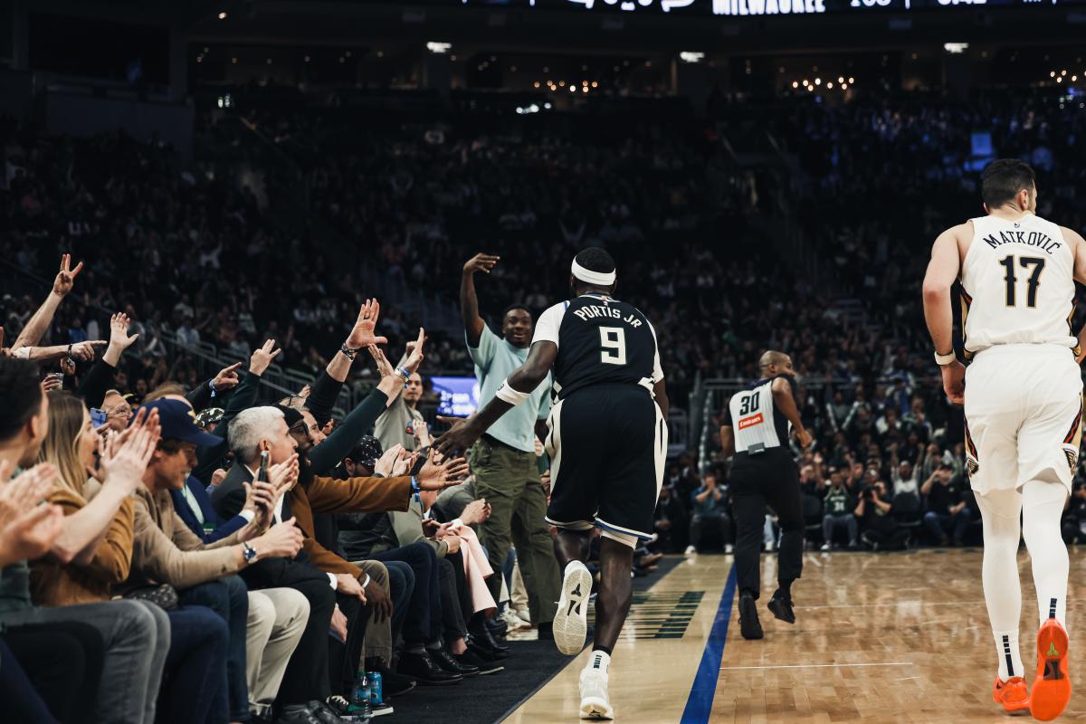 Milwaukee Bucks player Bobby Portis Jr. runs past the sideline at Fiserv Forum, exchanging high-fives with cheering fans as the crowd celebrates during a home game.