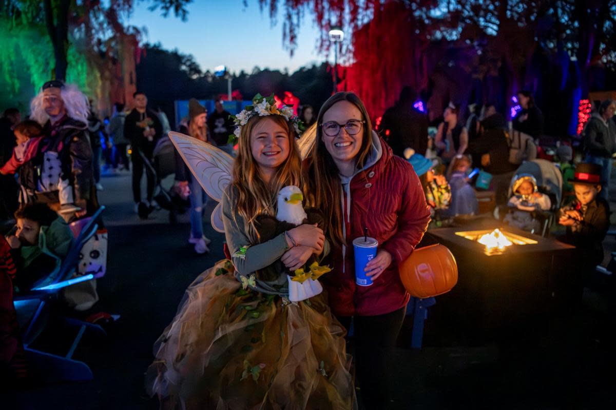 A girl in a fairy costume and a woman smiling together at a Halloween event, surrounded by families in costumes and festive lights during Boo at the Zoo.