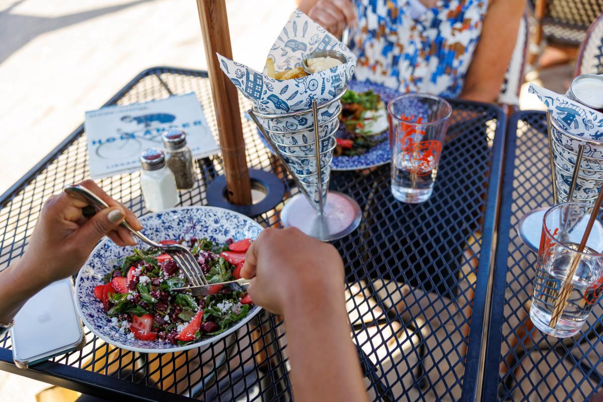 Diners enjoy a colorful salad and fries at an outdoor patio table.
