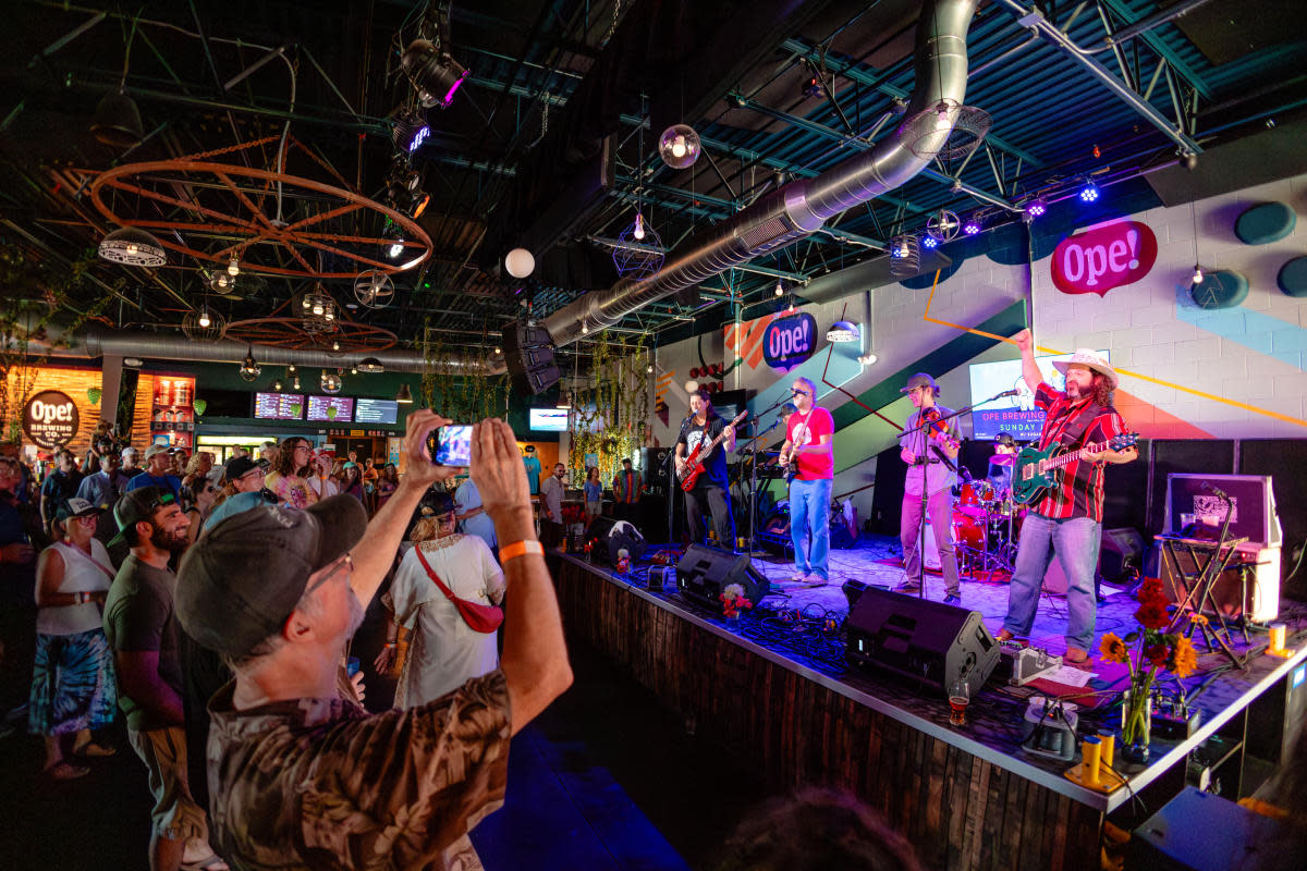 Live band performing on stage at Ope! Brewing Co. while a crowd gathers inside the colorful taproom to watch the show.