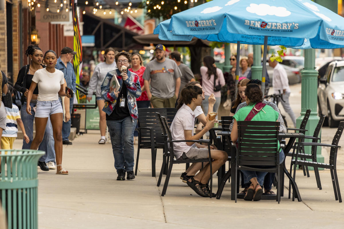 Visitors sit at colorful picnic tables and stroll through an outdoor dining area in Milwaukee’s Historic Third Ward, shaded by bright umbrellas and afternoon sunlight.