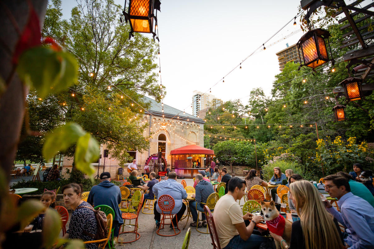 Lively outdoor patio at Colectivo Coffee on the Lake with colorful chairs, string lights, trees, and people dining under evening light.