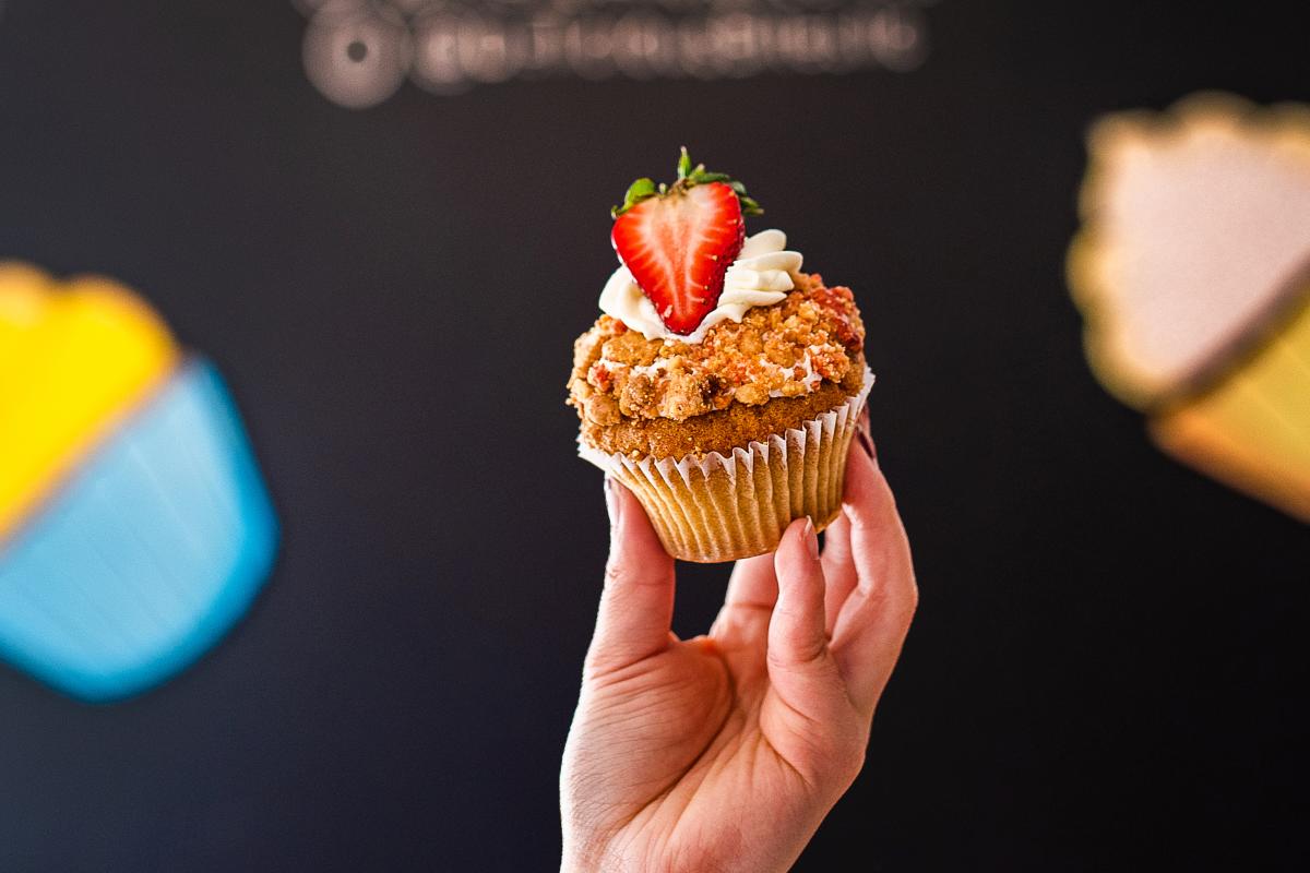 a hand holding up a cupcake with a strawberry on top