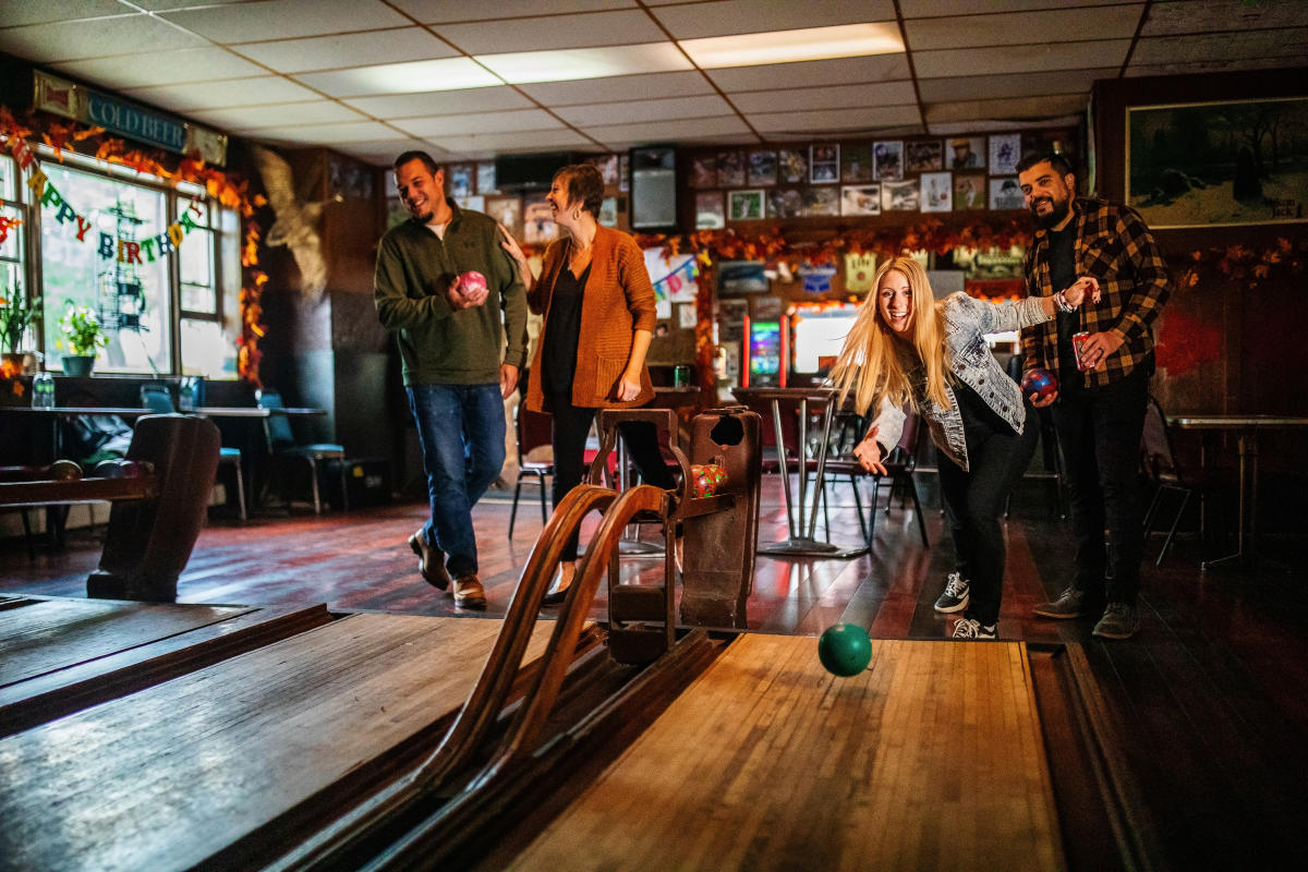 one person bowling in front of their friends in a dimly lit bowling alley