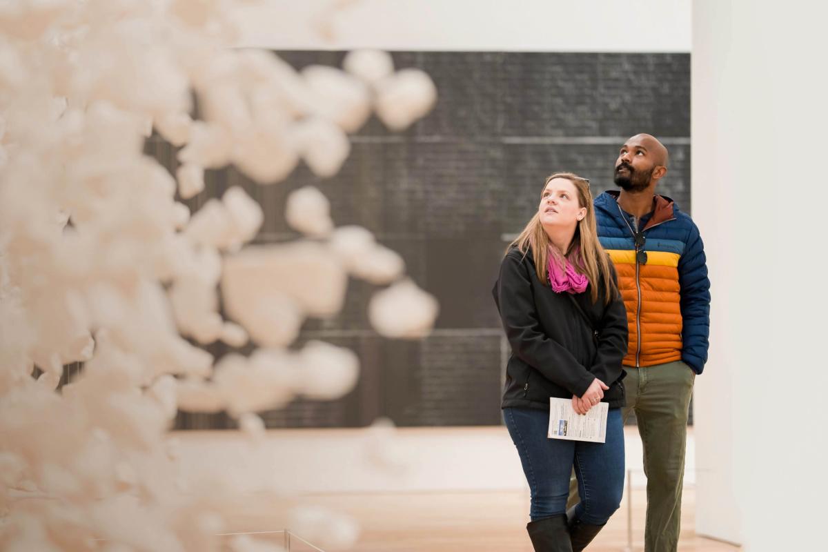 A couple walking through a museum exhibition staring wondrously upwards toward the show pieces