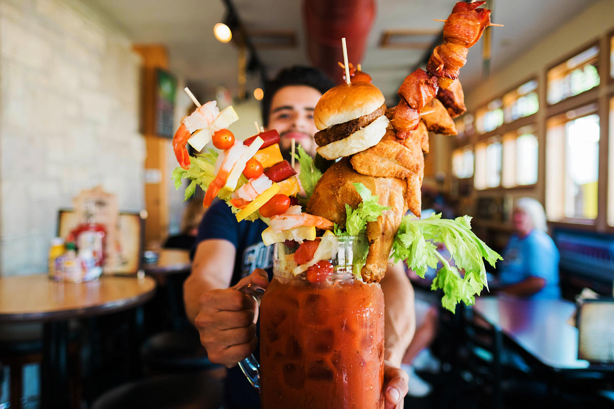bartender showing huge bloody mary with burger and other food