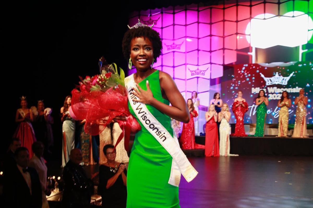 Willow Newell looks surprised at the front of a stage holding flowers and wearing a sash that says Miss Wisconsin