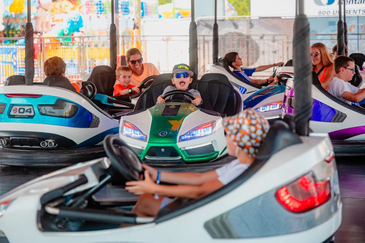 Children and adults smile and laugh while steering colorful bumper cars around the ride pavilion at the Wisconsin State Fair.
