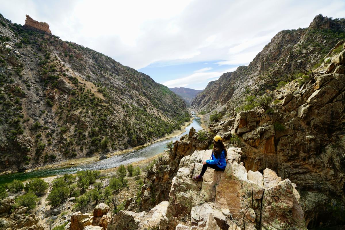 Hiker sits on a rock overlooking a stretch of the Gunnison River in the Gunnison Gorge