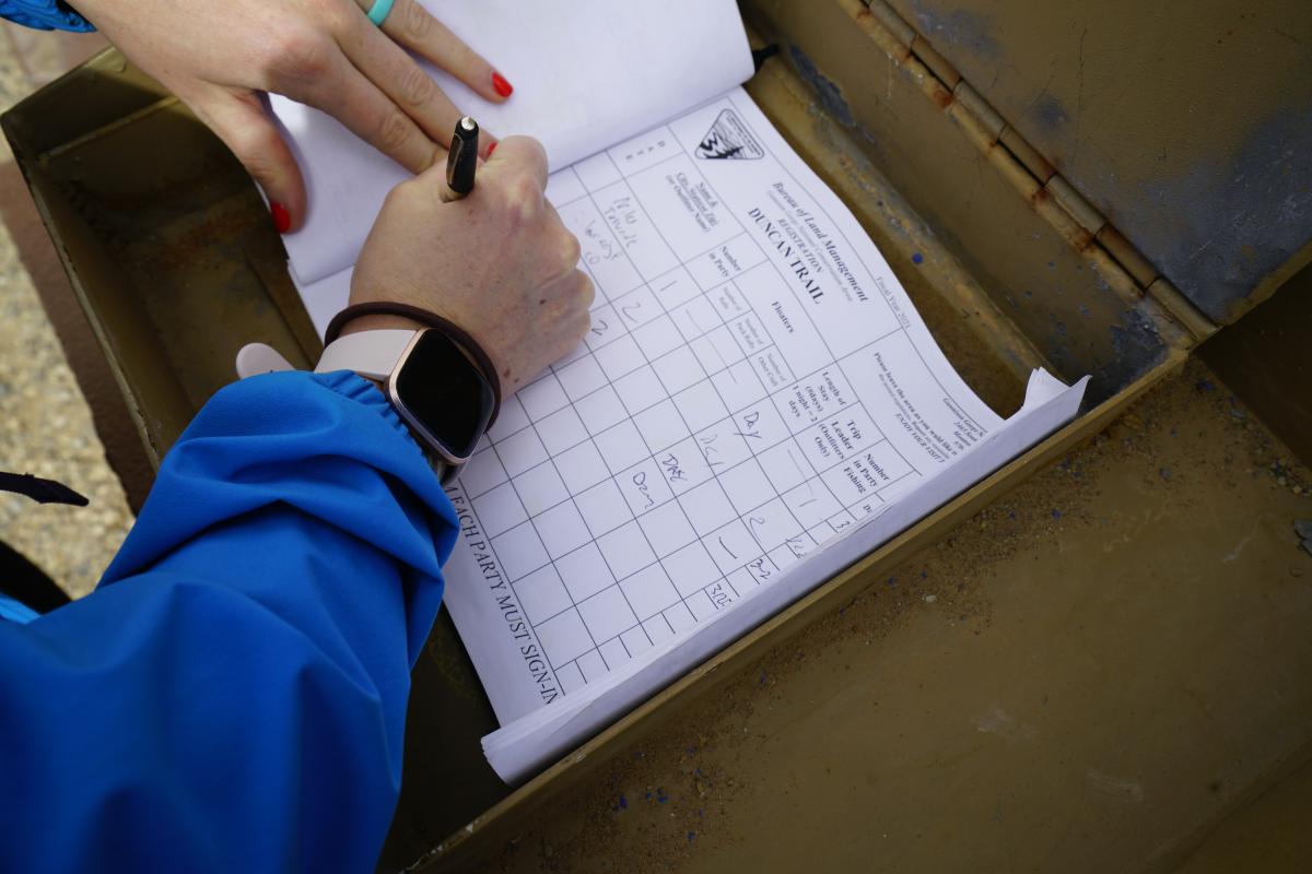 A close up shot of a hiker's hands as she signs in on the Duncan Trail registration log.