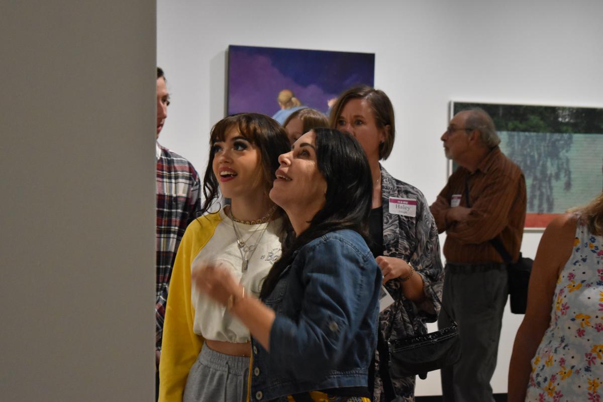 wo people excitedly observing artwork in the Muskegon Museum of Artfilled with other visitors.