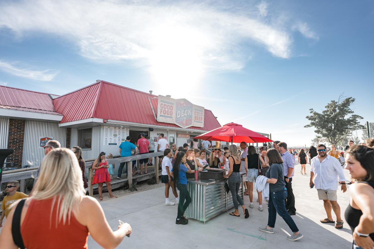 A bustling scene at The Deck, an outdoor venue with people socializing under a bright sky.