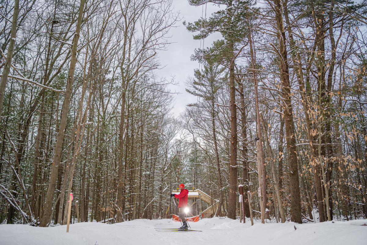 person in red winter coat cross country skiis over snow covered trail at Muskegon Luge Adventure Sports Park