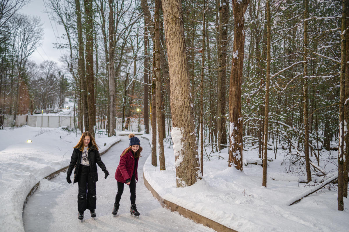 two young girls ice skate on trail through woods.