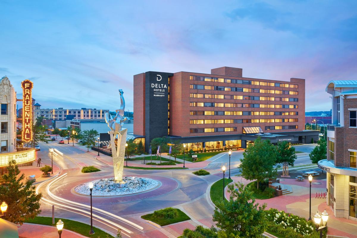 View of the Delta Hotels building and Frauenthal theater at twilight with a circular road and central statue in the foreground.