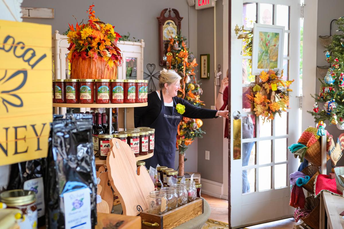 smiling woman opens door to her shop that is decorated for fall