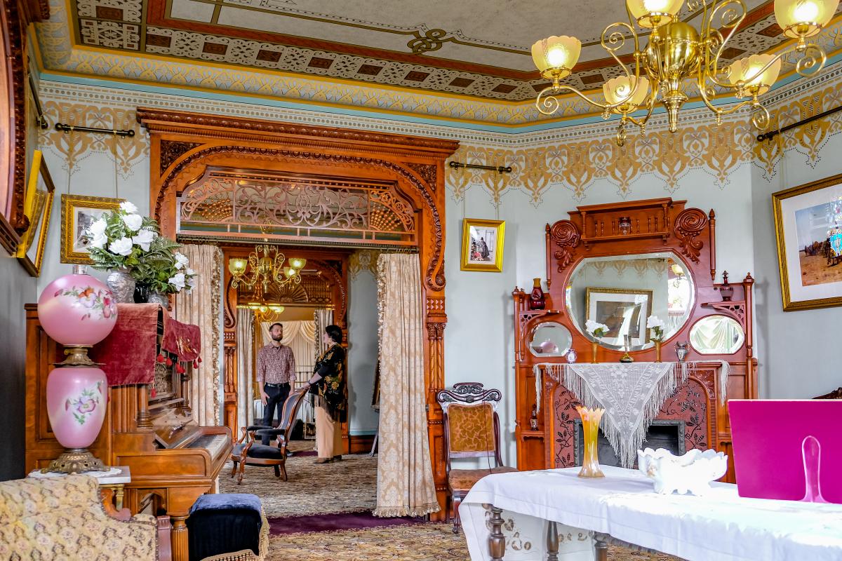 Interior view of the elaborately decorated Hackley House parlor, featuring vintage furnishings, ornate wood carvings, and elegant chandeliers.