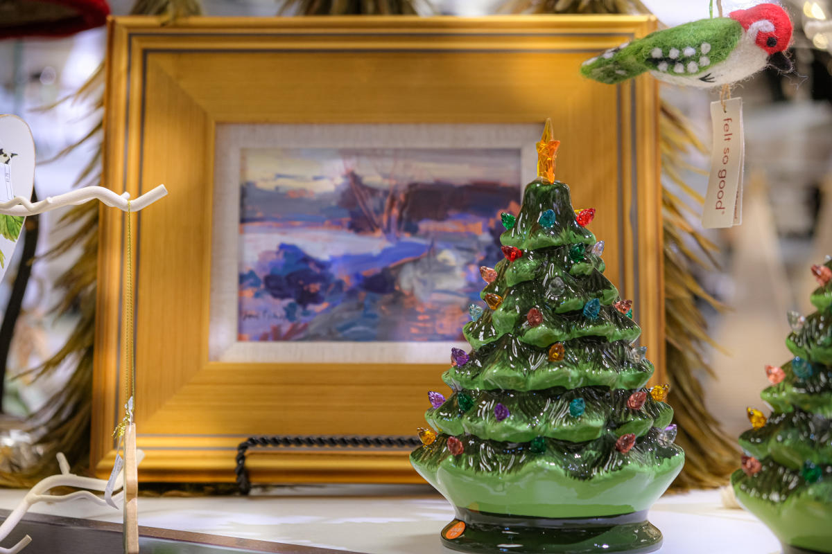 A decorative ceramic Christmas tree with colorful lights on display, flanked by a framed landscape painting and a small bird ornament on the left.