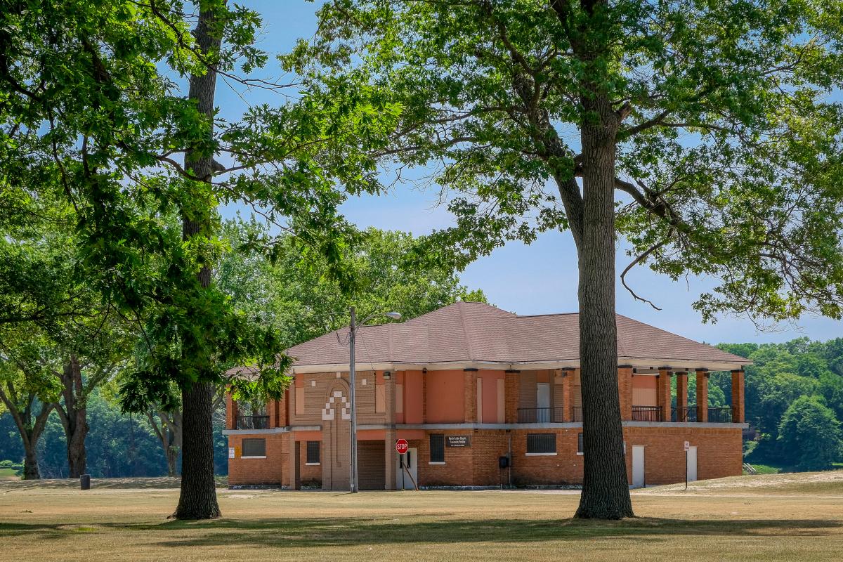 Mona Lake Park Pavillion can be seen in front of inland lake with green trees filling the right of the fram