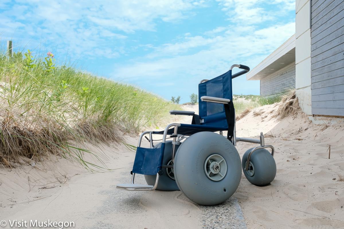 Beach Wheel Chair sits on sand covered trail between beach bath house and beach grass