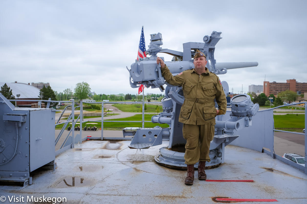 WWII reenactor in WW2 outfit stands before A three-inch 50 caliber naval gun on deck of USS LST 393 museum
