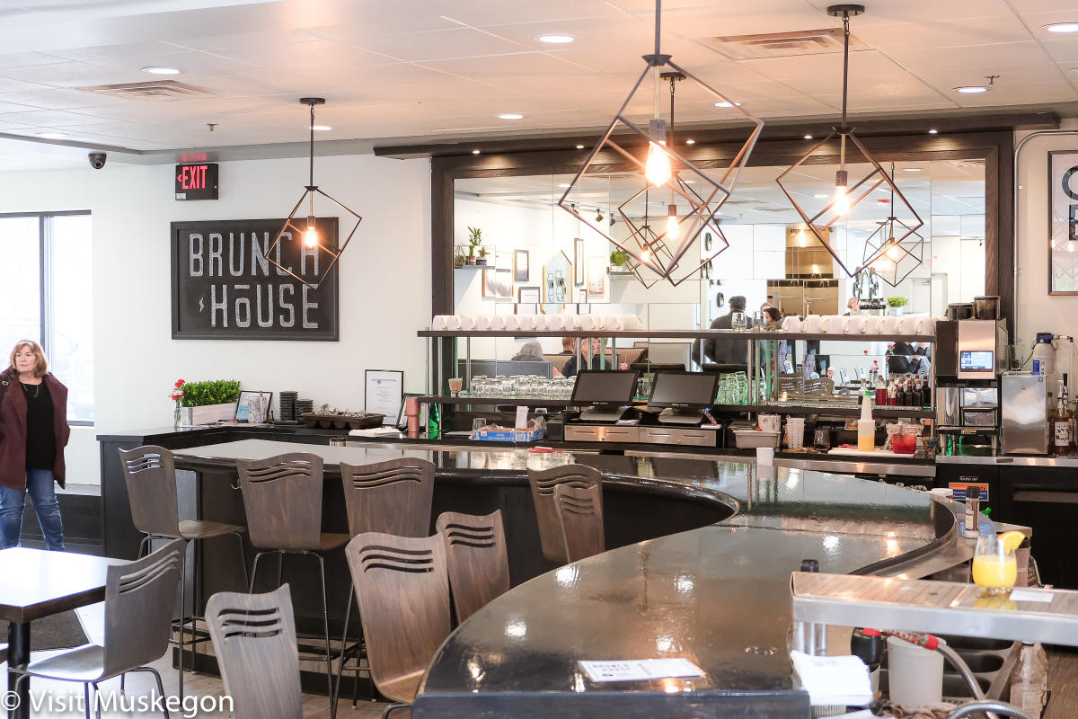 curved counter in brunch restaurant. modern light fixture sparkle overhead. shiny mirror sets background for bar area. sign to left reads brunch house.