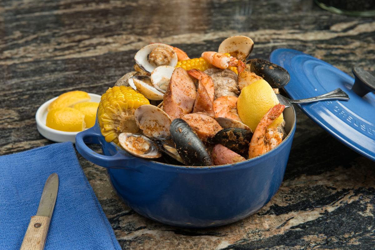 A large blue pot filled with a seafood boil that include oysters, shrimp, mussels and corn on the cob