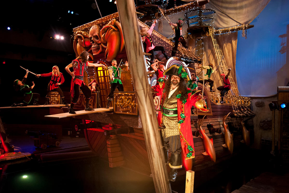 A pirate stands in front of a pirate ship where we see numerous swordfights during the Christmas at Pirates Voyage show