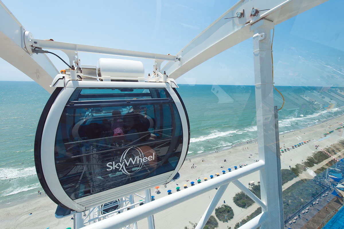 A young girl stands looking out the window of the Skywheel as it climbs above the beach in Myrtle Beach