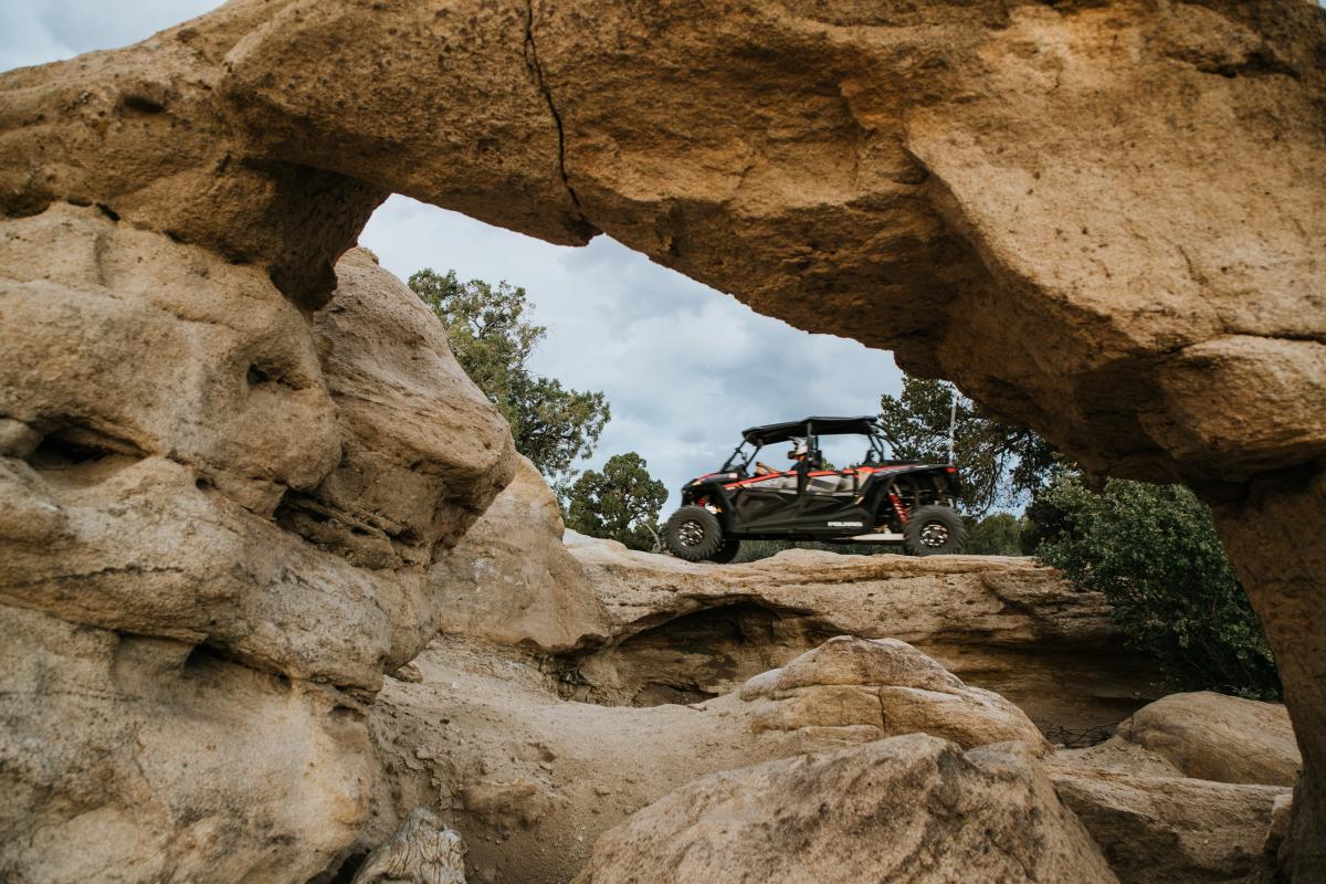 An off-road vehicle is silhouetted by a stone arch while it drives along a rocky surface