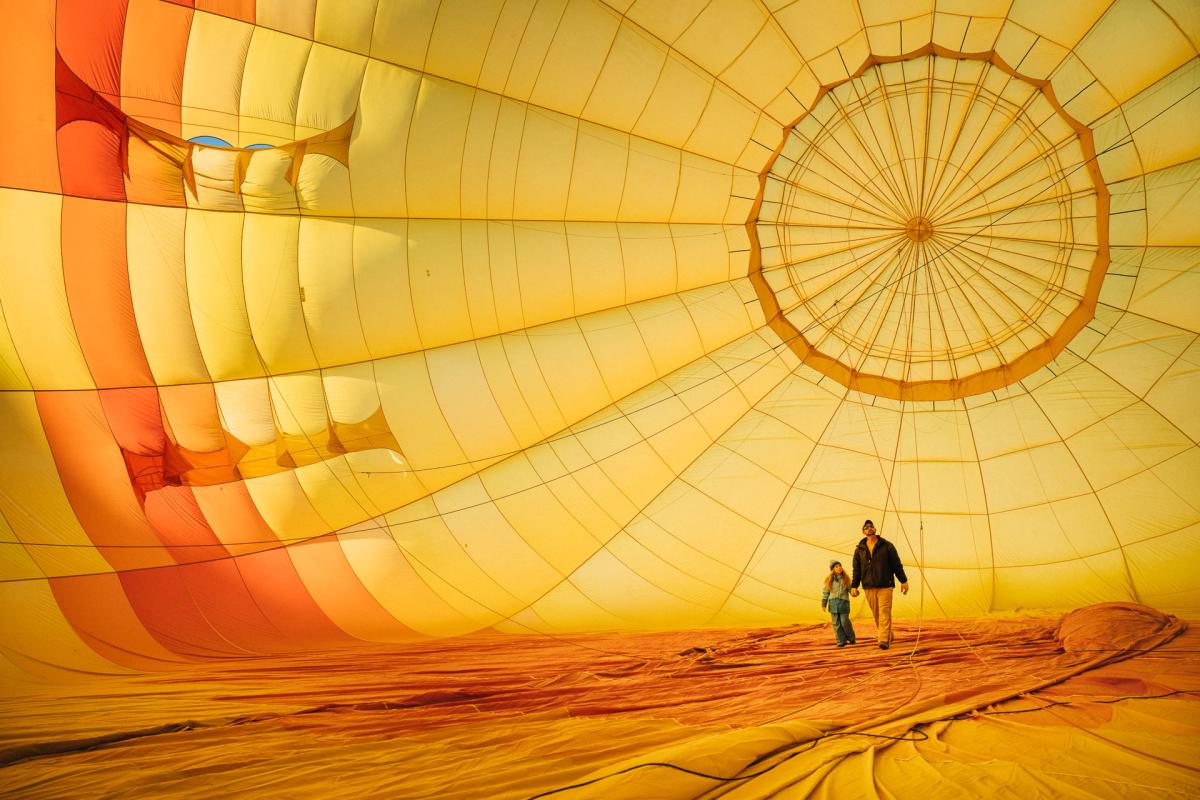Two individuals holding hands while walking inside a partially inflated hot air balloon