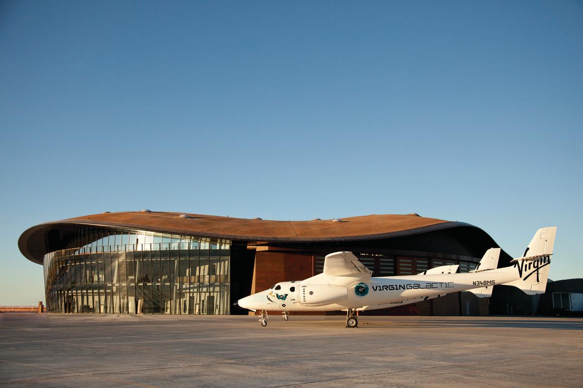 A plane sits in front of a futuristic building with a clear sky overhead
