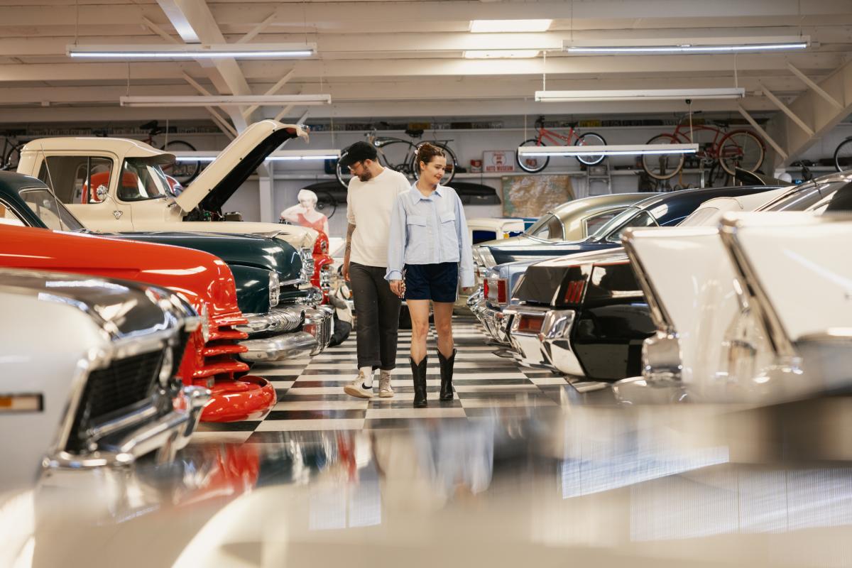 Two individuals walking through a vintage car exhibition, inspecting classic models closely.