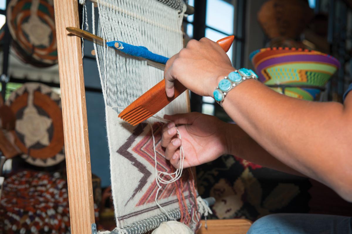 A weaver weaving on a vertical loom at the New Mexico Fiber Crawl