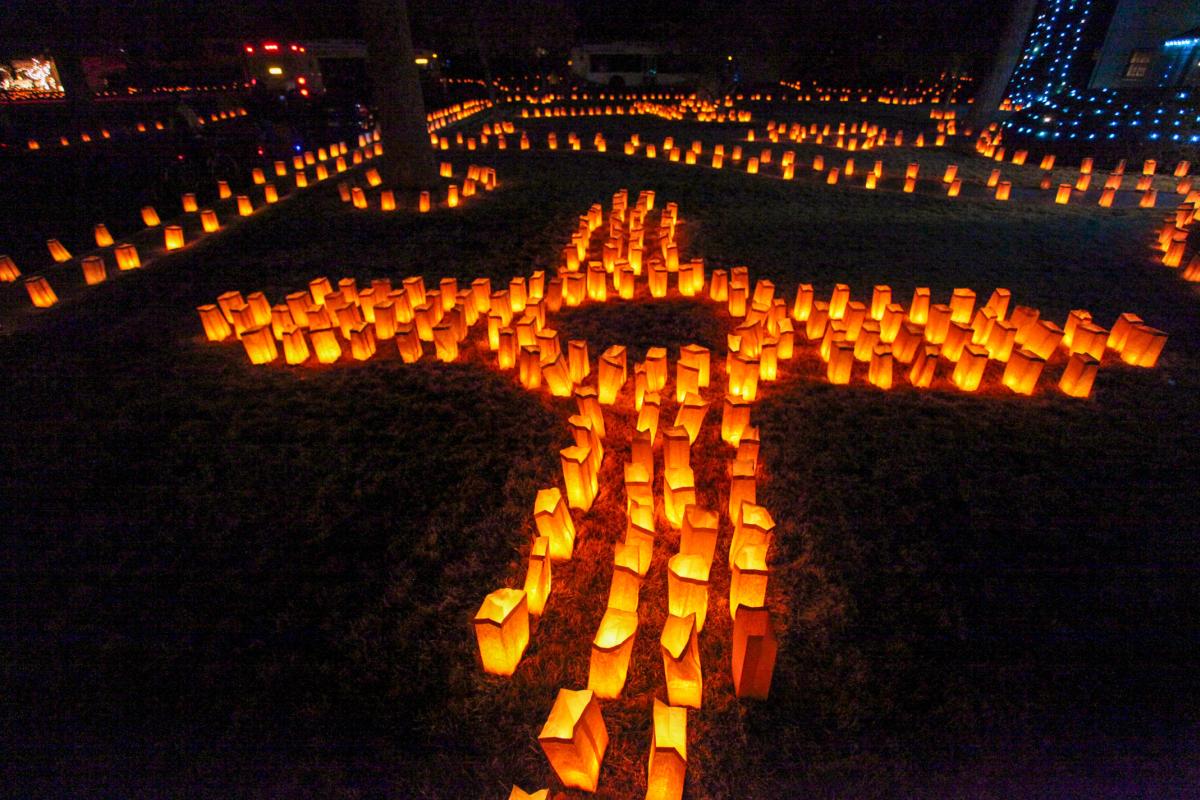 Nighttime view of numerous luminarias arranged to form a large cross, illuminating the area with a soft, warm glow.