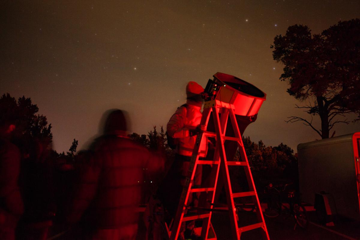 A person stands on a ladder looking through a large telescope at night